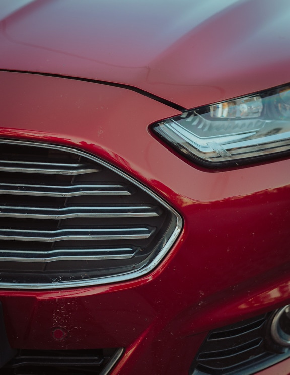 Close-up of headlight and bumper of dark red metallic sports car