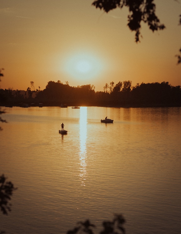 Silhouette of fisherman in fishing boat on lake in sunrise