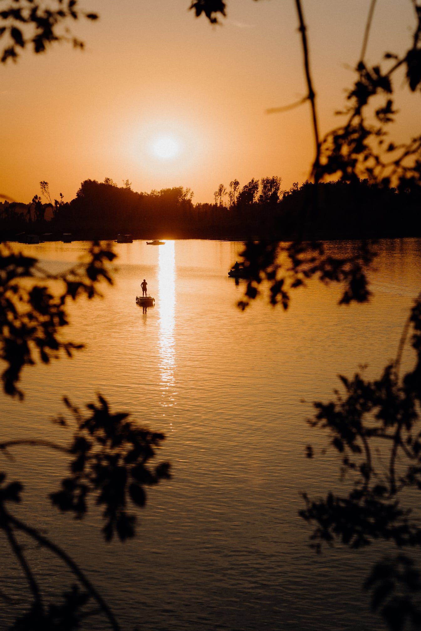 Kalastusveneessä seisovan kalastajan siluetti oranssinkeltaisessa auringonlaskussa