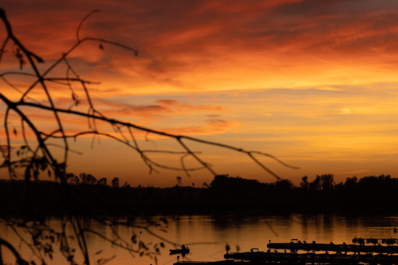 Oranssinkeltainen taivas auringonlaskun aikaan ja panoraama järven rannalla