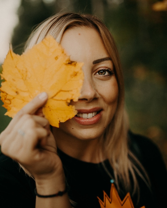 Potret model foto cantik tersenyum dengan daun kekuningan di tangan
