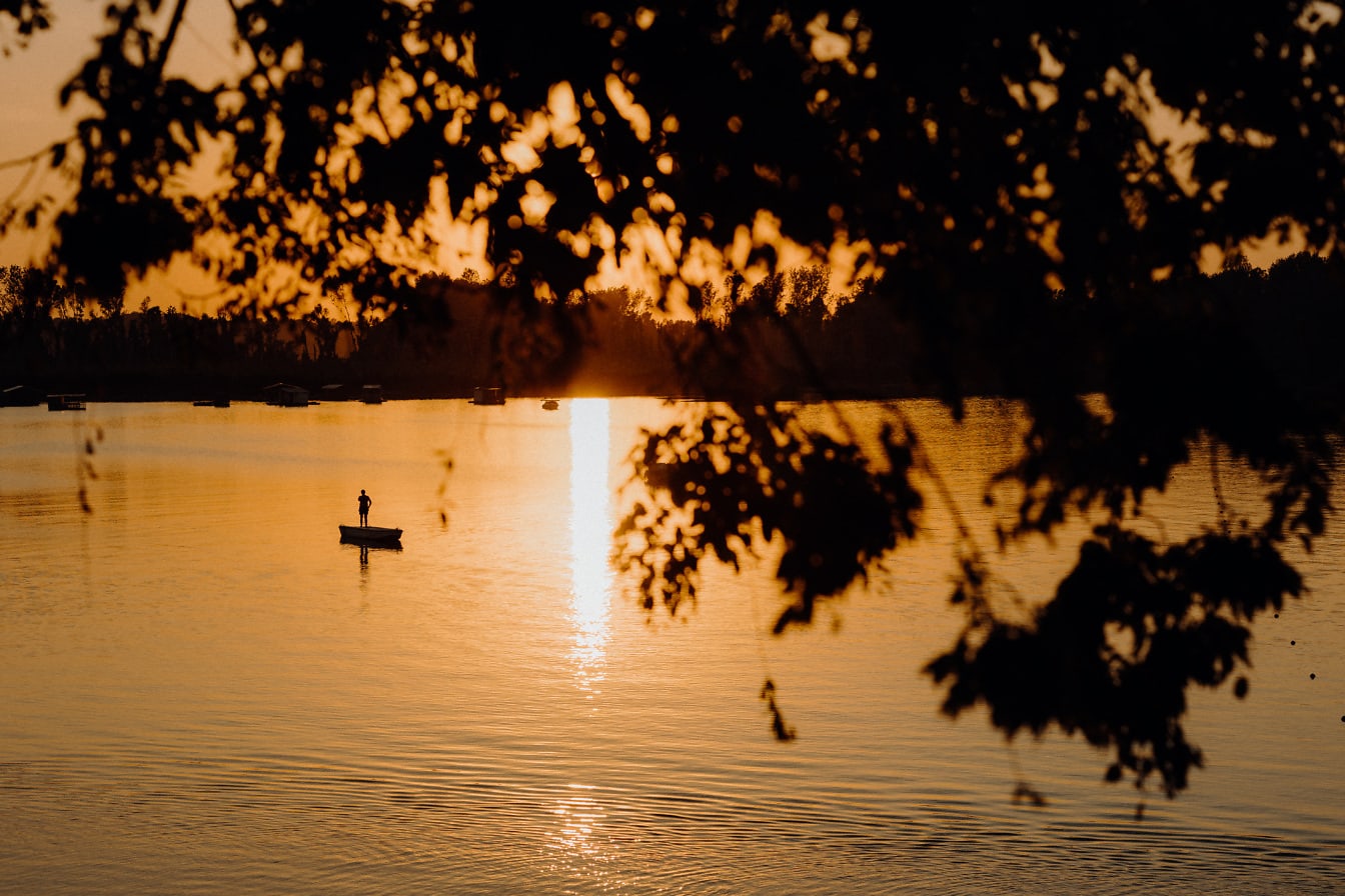 Silueta de la persona de pie en el barco en la distancia en la puesta del sol