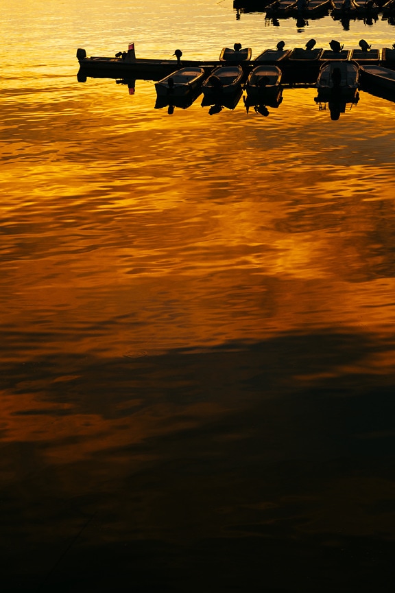 Majestic orange yellow sunrise on lake harbor with silhouette of fishingboats