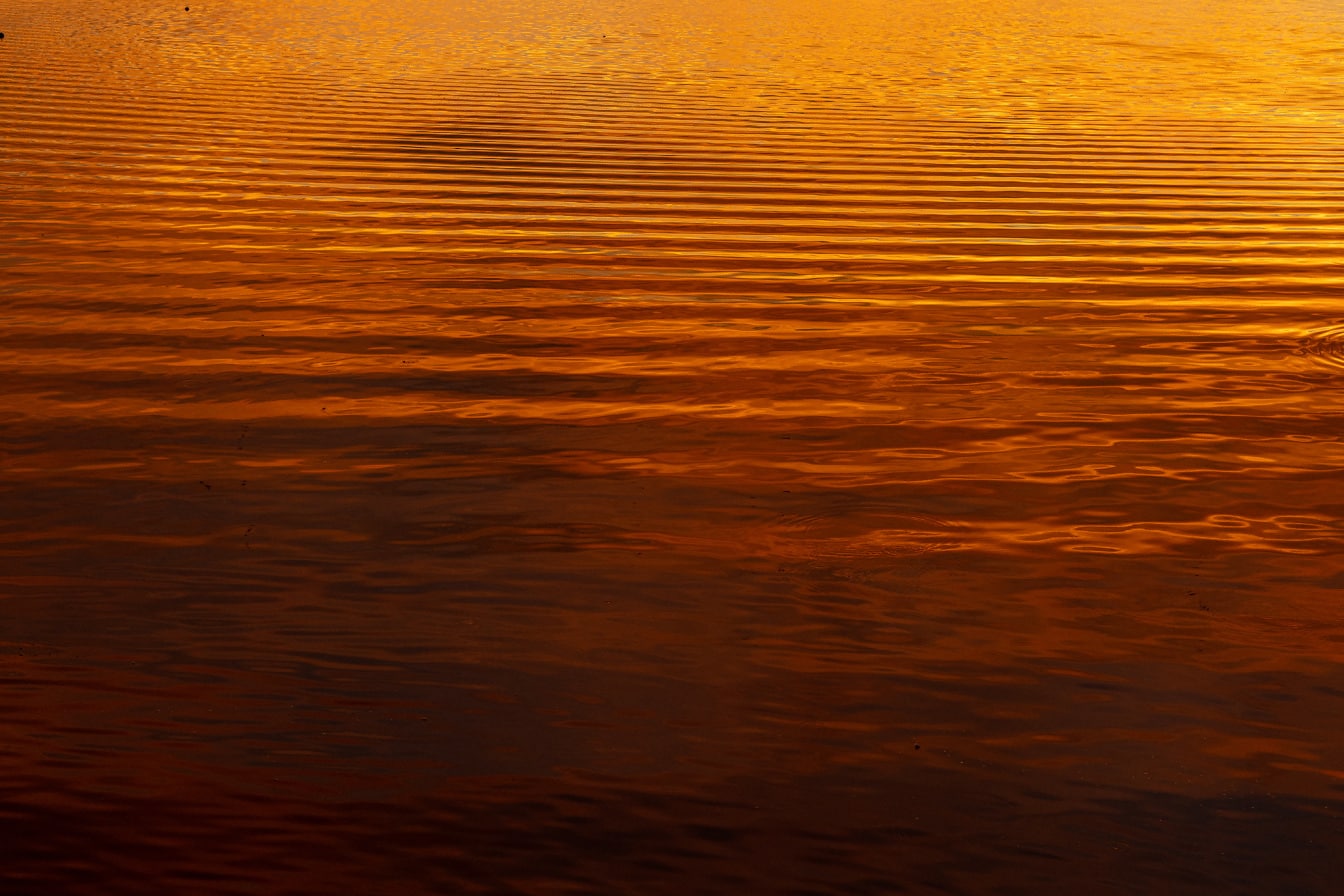 Tmavě oranžově žlutý odraz na vodních vlnách při západu slunce