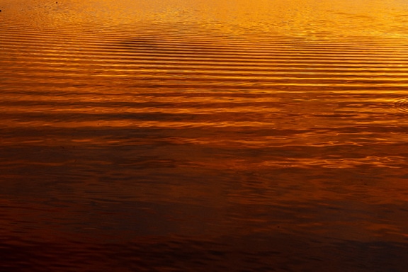Dark orange yellow reflection on water waves in sunset