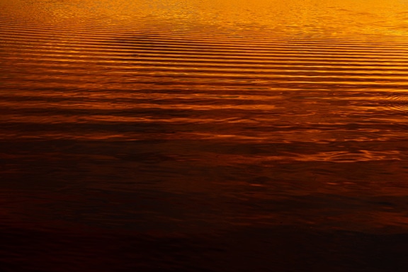 Dark red and orange yellow reflections on waves of calm water in sunrise
