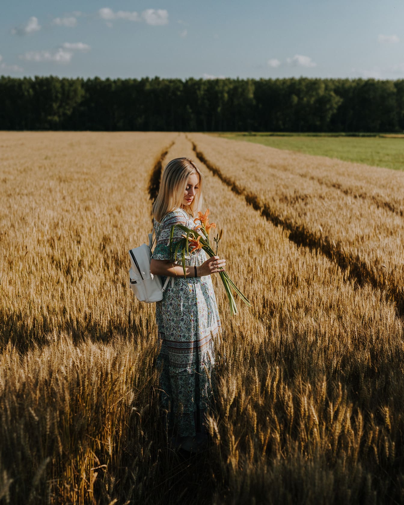 Hermosa mujer joven de cabello rubio con flores en el campo de trigo
