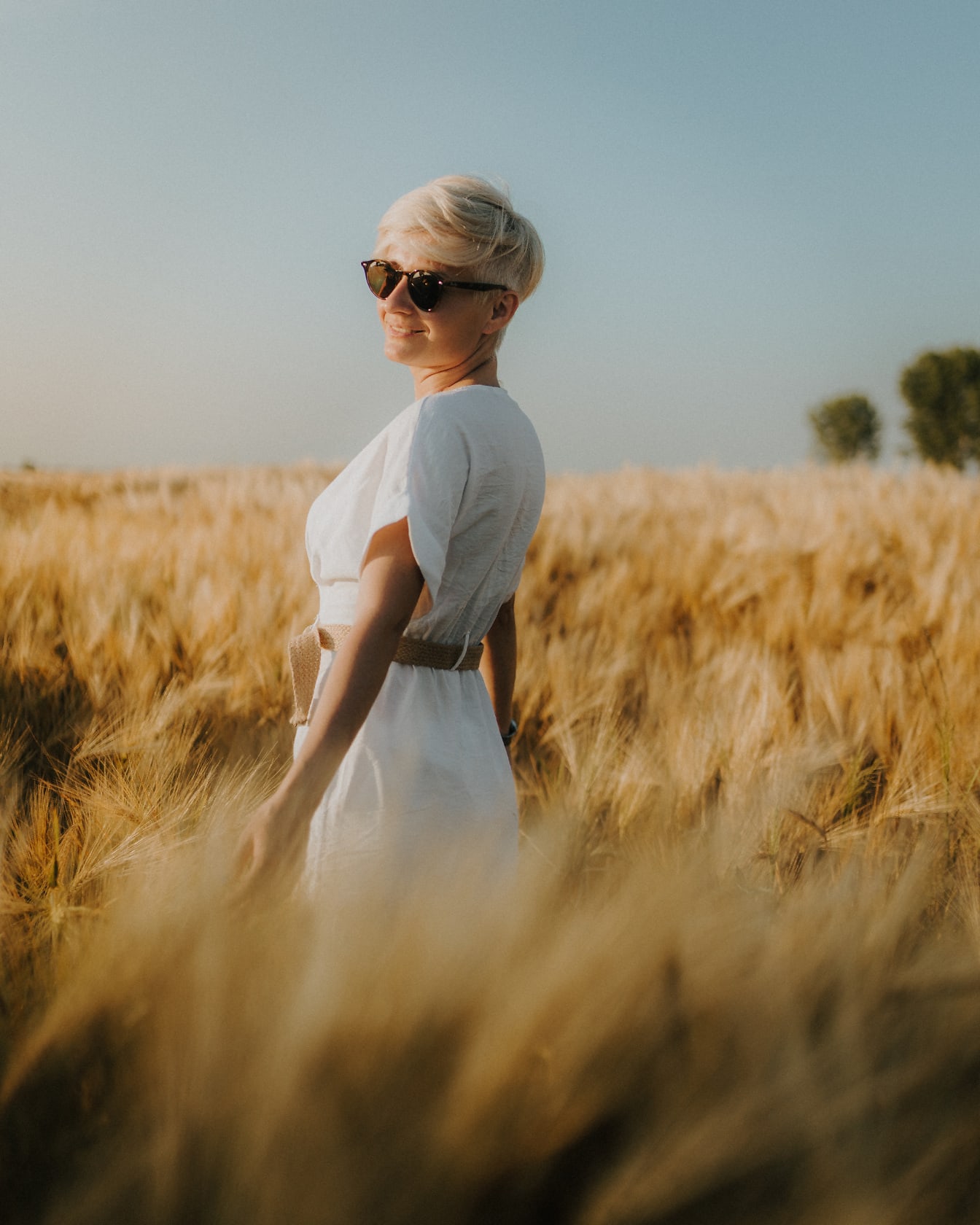 Красива руса коса жена в бяла рокля в пшенично поле