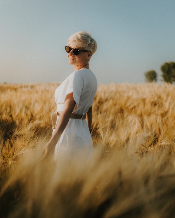 Hermosa mujer de pelo rubio en vestido blanco en campo de trigo