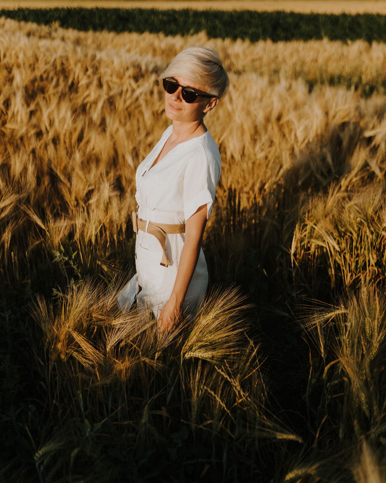 Donna graziosa con occhiali da sole e vestito bianco nel campo di grano in estate