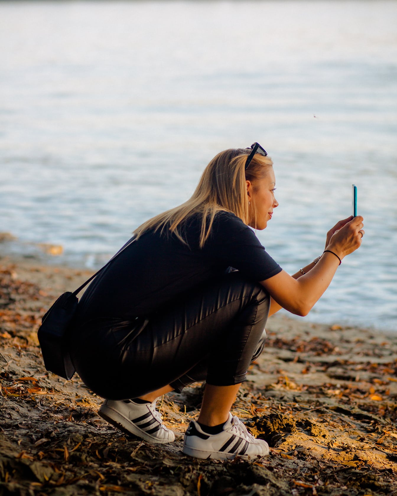 Блондинка в черных кожаных штанах фотографируется на мобильный телефон