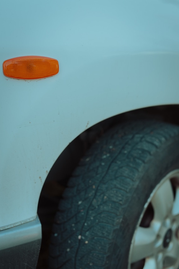 Tampilan close-up plastik blinker kuning oranye pada mobil dan ban