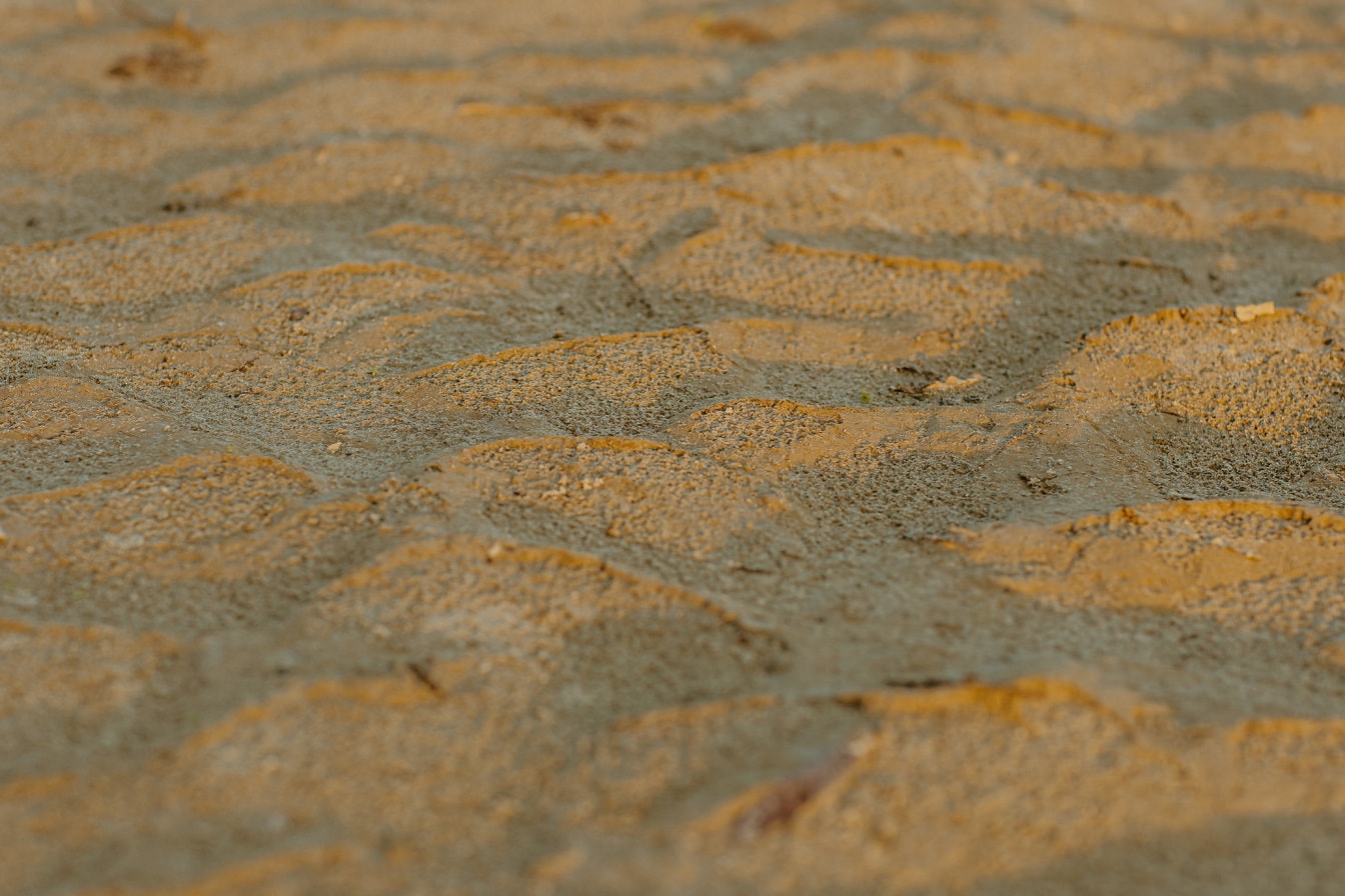 Nahaufnahme der Textur von gelblichem Sand mit Sonnenschatten
