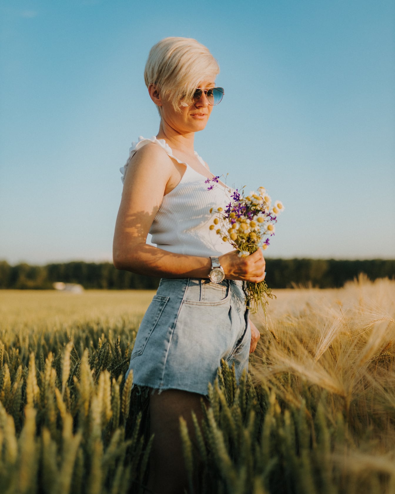 Шикарна блондинка з коротким волоссям з букетом квітів на пшеничному полі