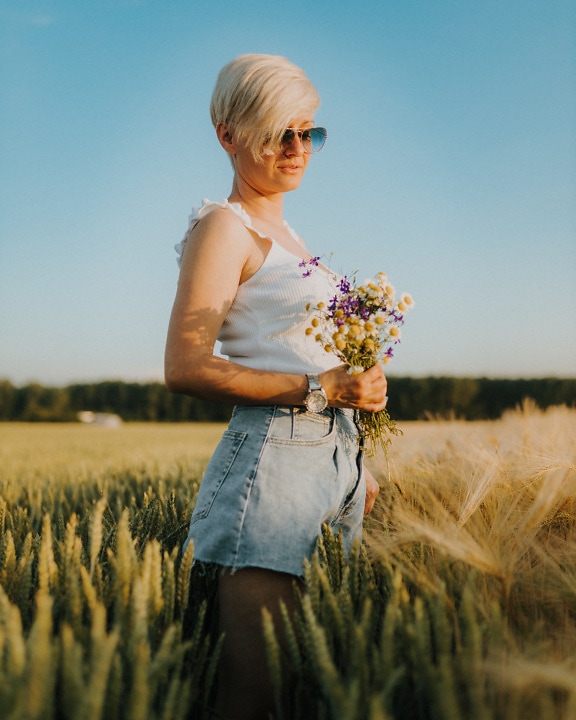Gorgeous short hair blonde with bouquet of flowers in wheat field