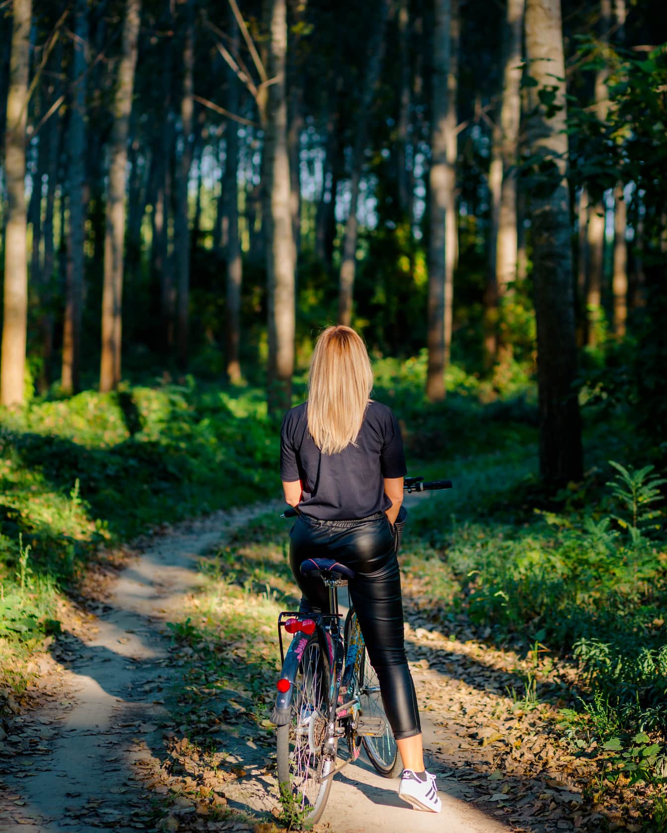 Adolescente dai capelli biondi in bicicletta sulla strada forestale