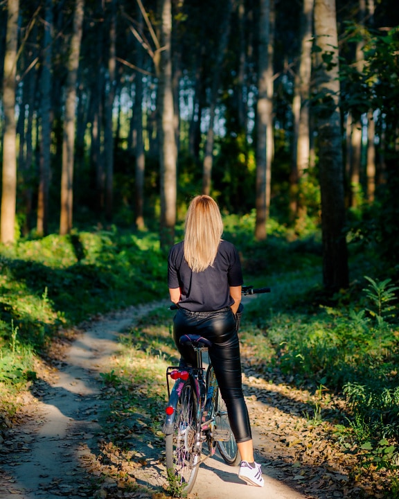 Blonde hair teenager on bicycle on forest road