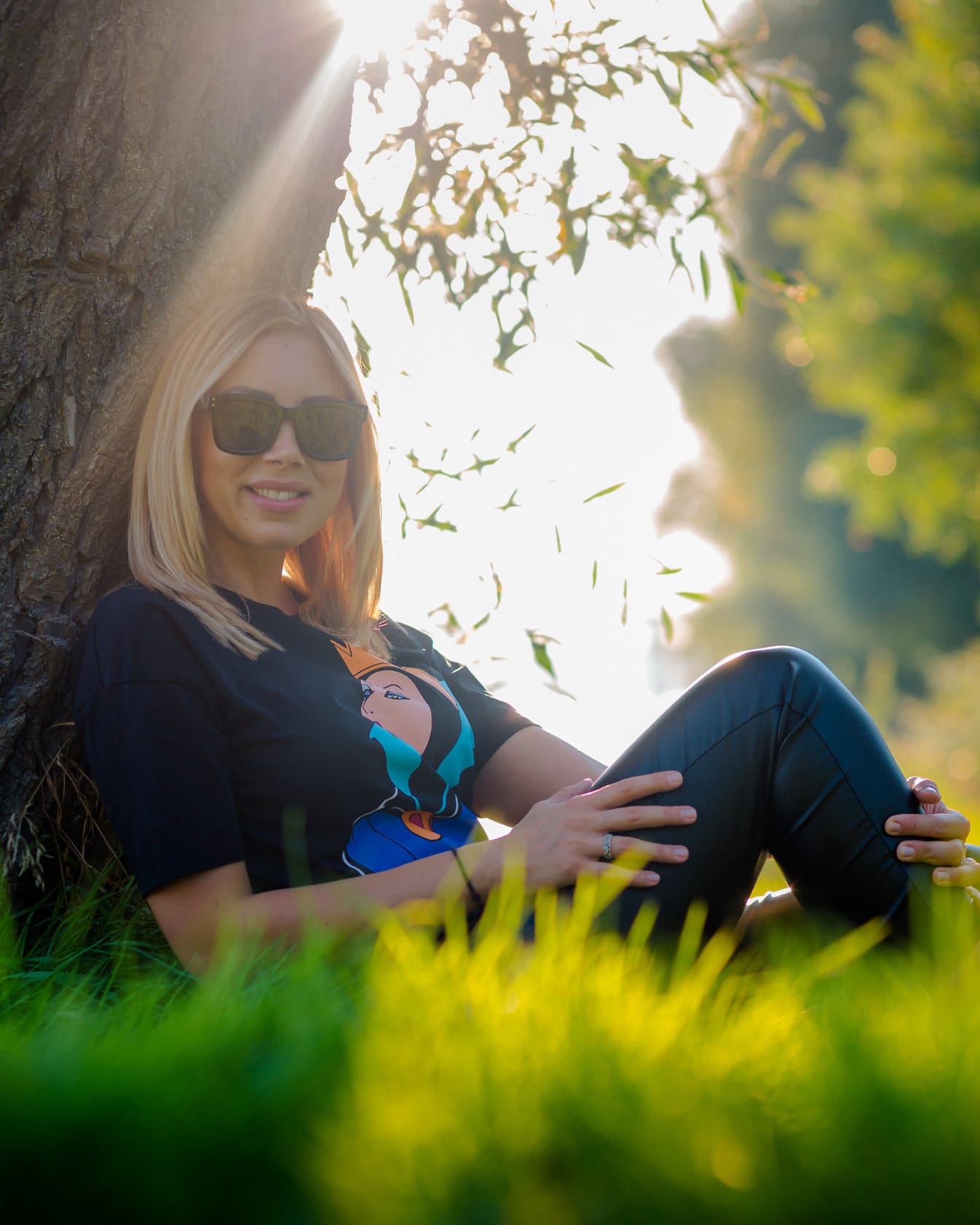 Casual porträtt av blond hårkvinna som sitter under trädstammen