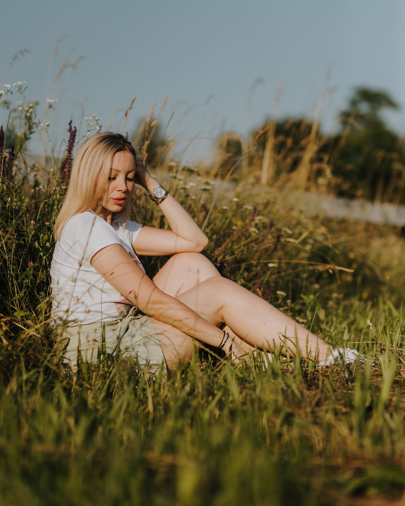 Wanita muda berambut pirang cantik duduk di padang rumput