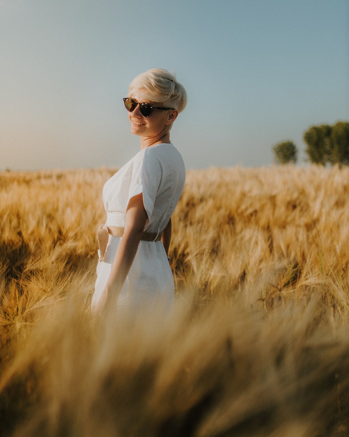 Femeie blondă fericită în rochie albă în lan de grâu