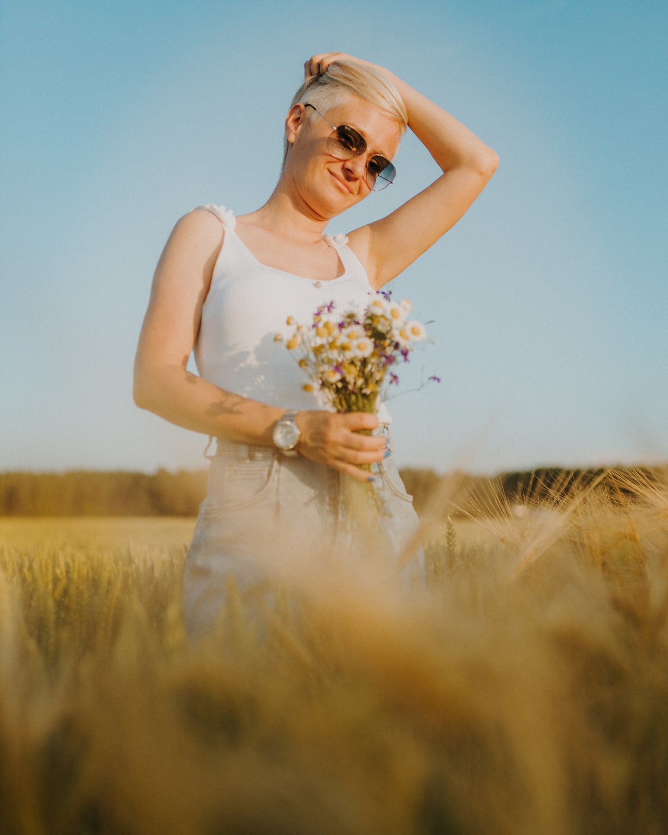 Hermosa mujer en camisa blanca con flores posando en campo de trigo