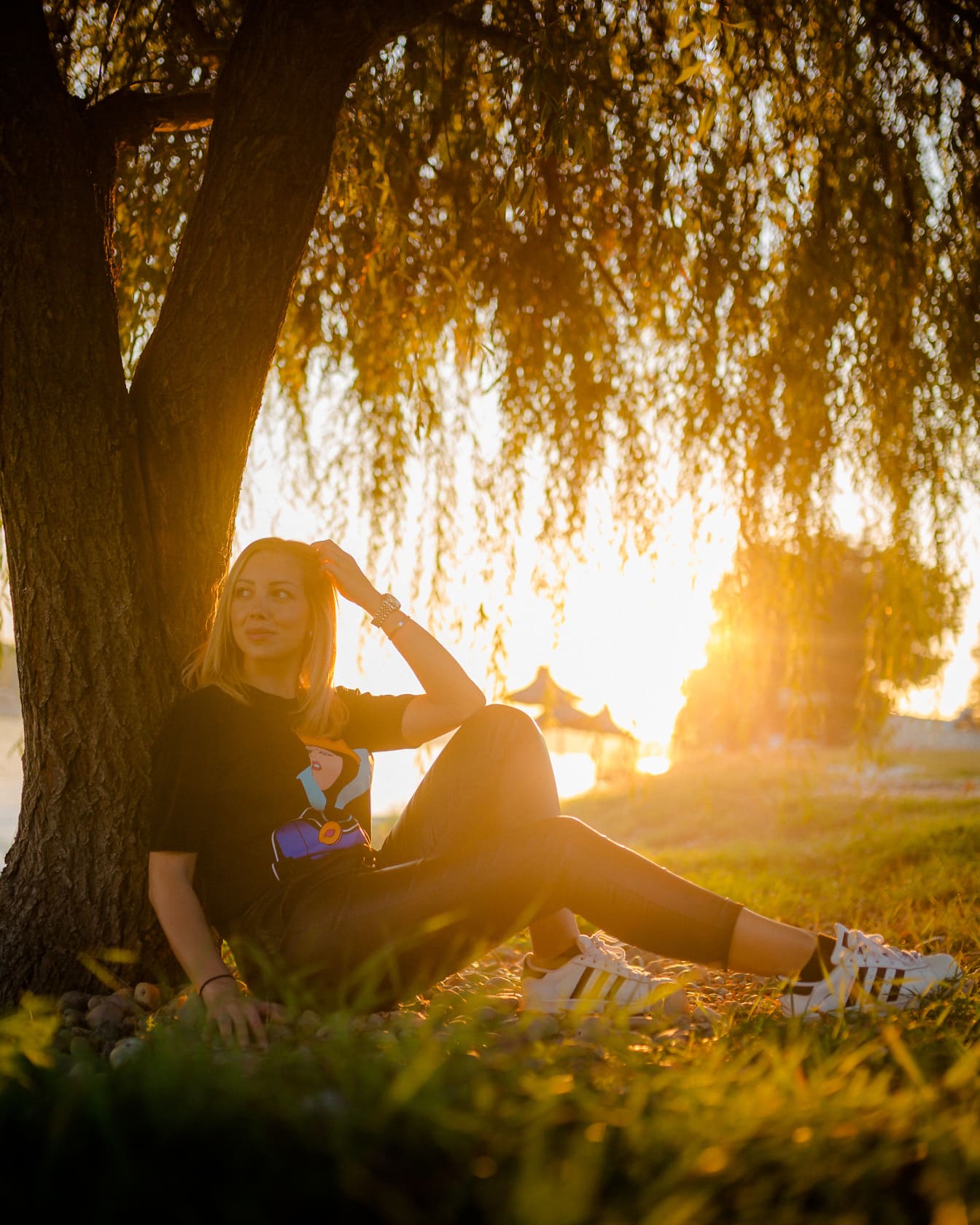 Hezká dospívající dívka sedí pod stromem při západu slunce se slunečními paprsky v pozadí