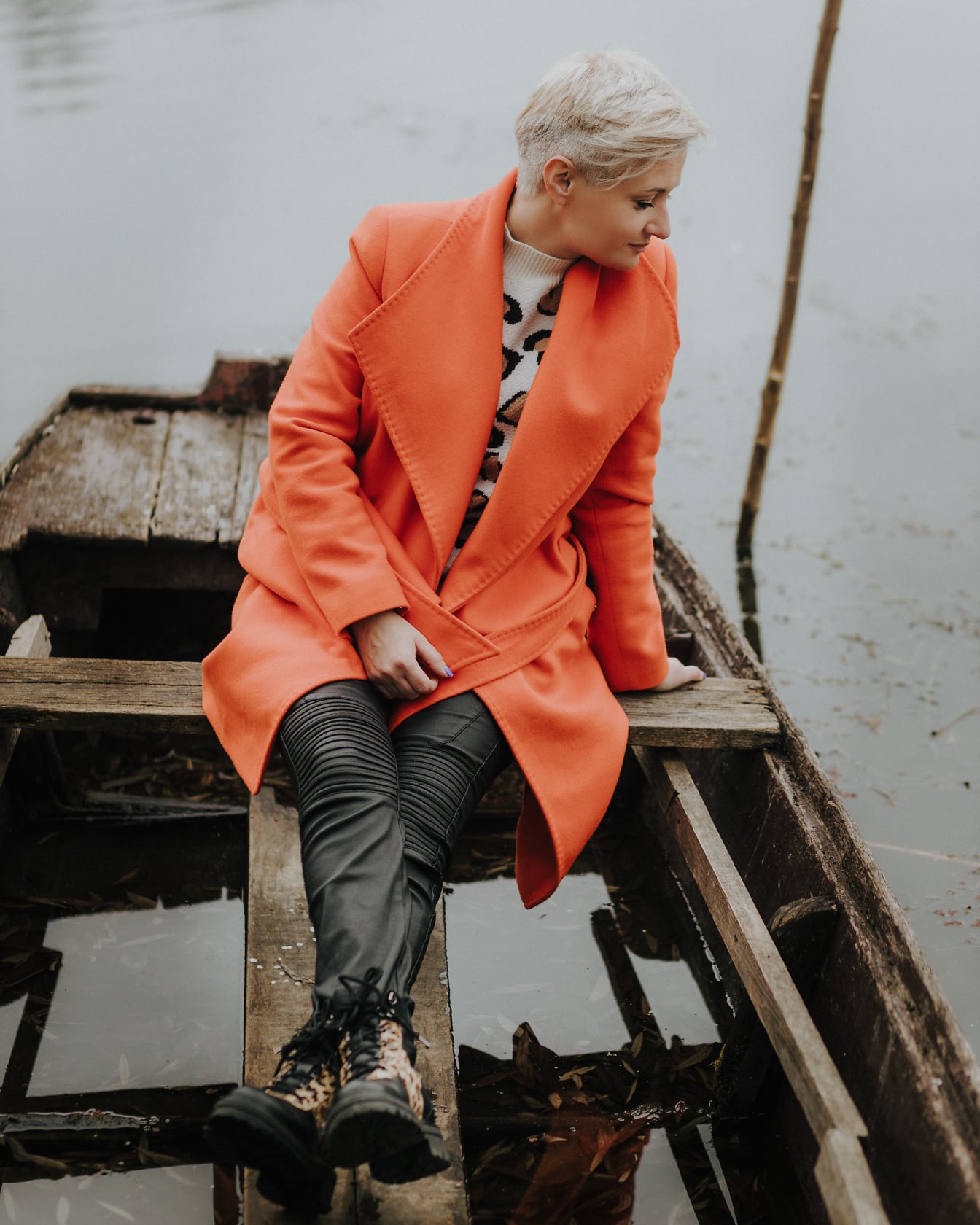 Blondýnka sedí v dřevěné lodi v podzimním kabátě