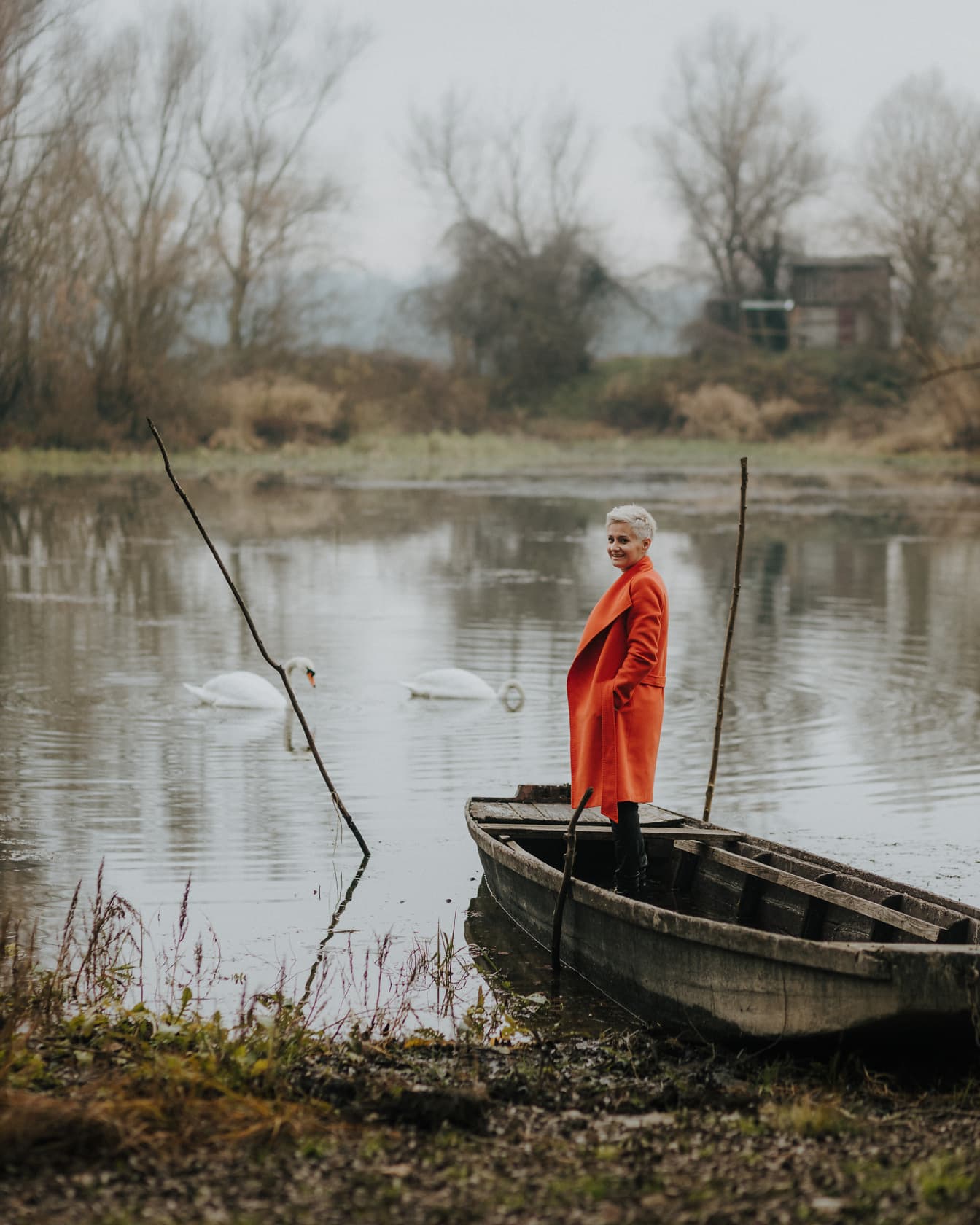 Hübsche Frau, die im Boot im orangegelben Mantel steht