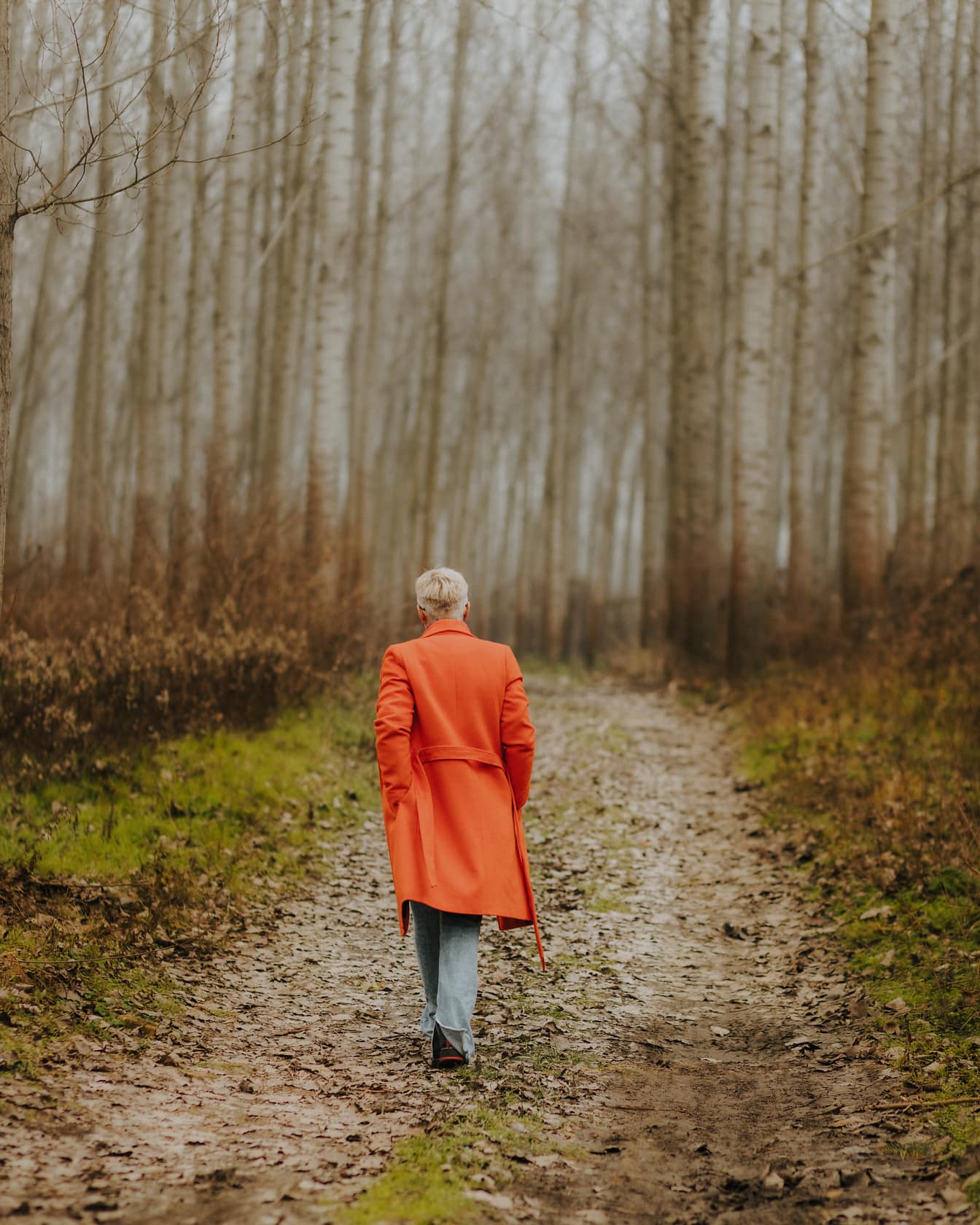 Woman walking in orange yellow coat on forest trail in autumn