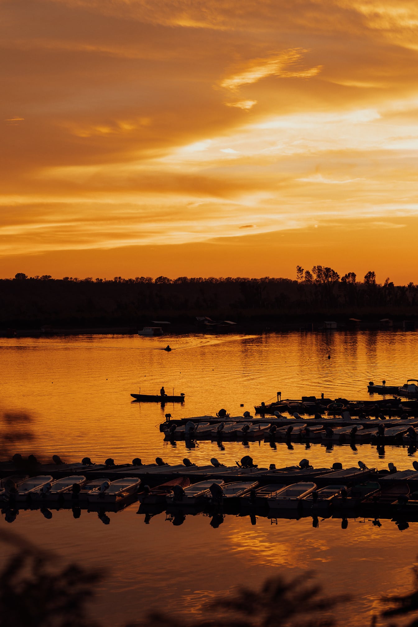 Reflexo majestoso do pôr do sol à beira do lago com silhueta de barcos no porto
