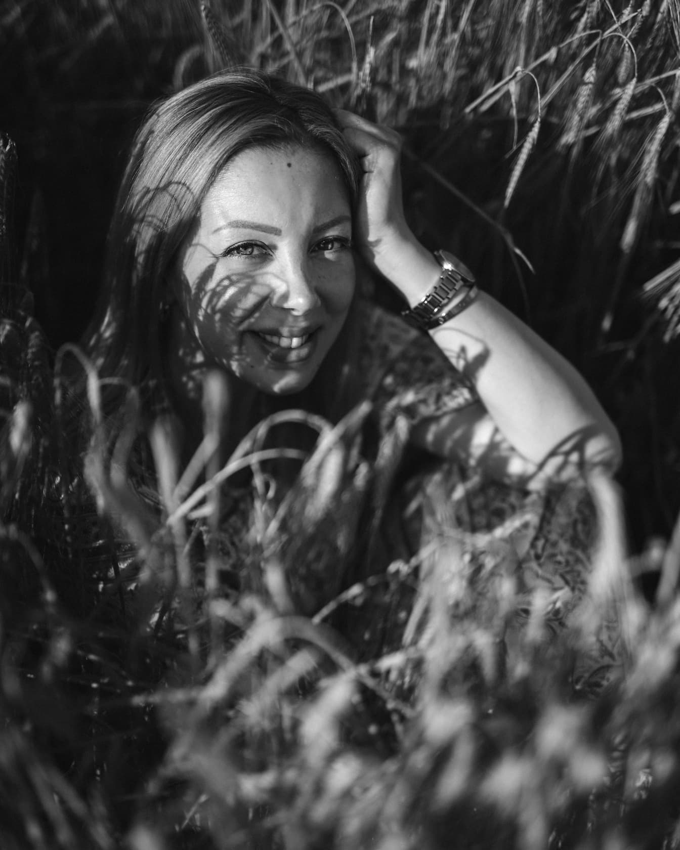 Mulher da fotografia do retrato da escala de cinza sentada no campo do trigo