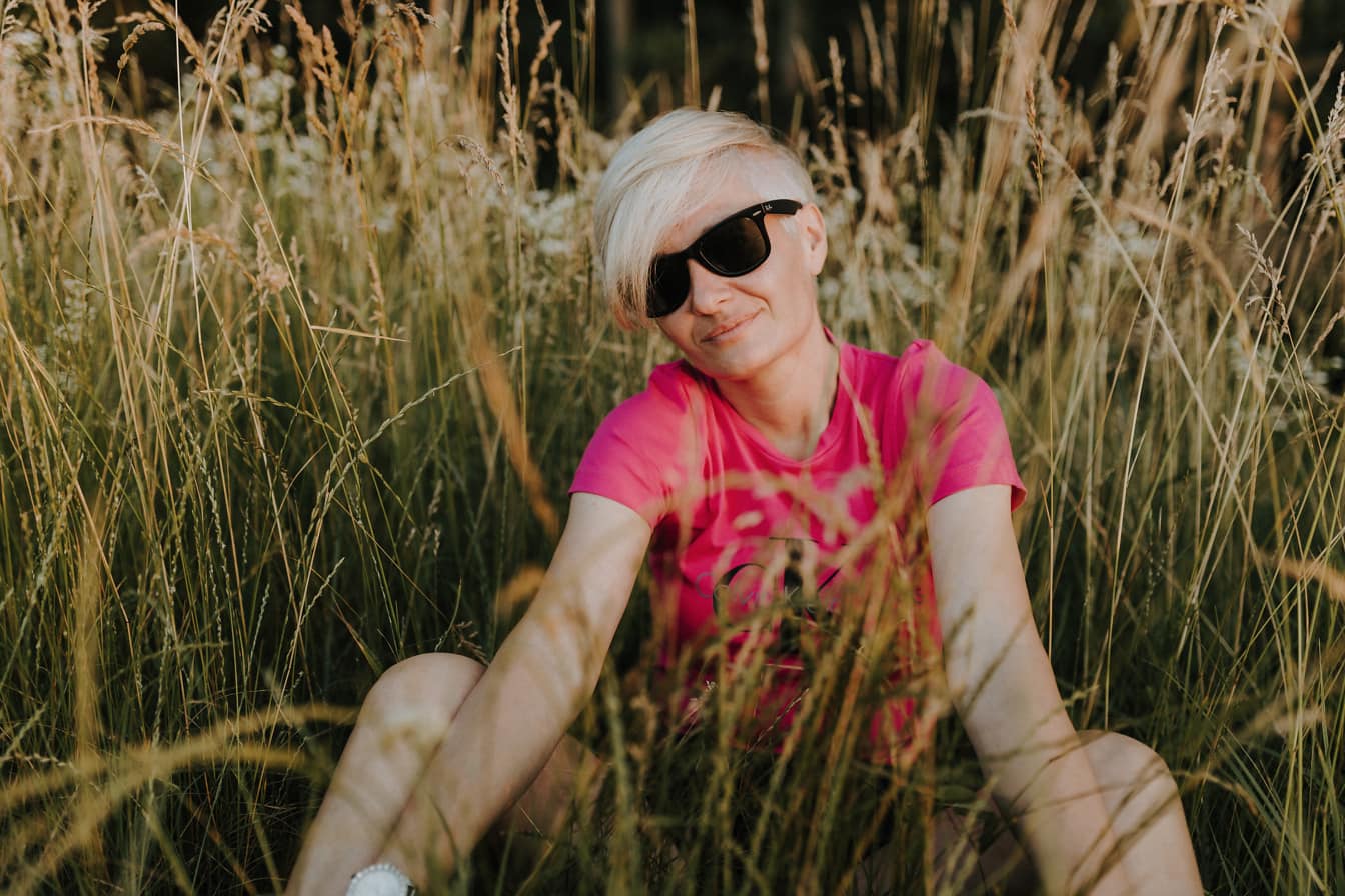 Przystojna blondynka w różowawej koszuli siedzi w trawie