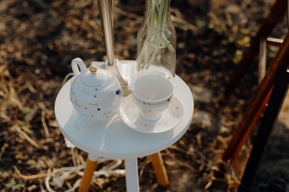 White porcelain mug and tea kettle on wooden tripod table