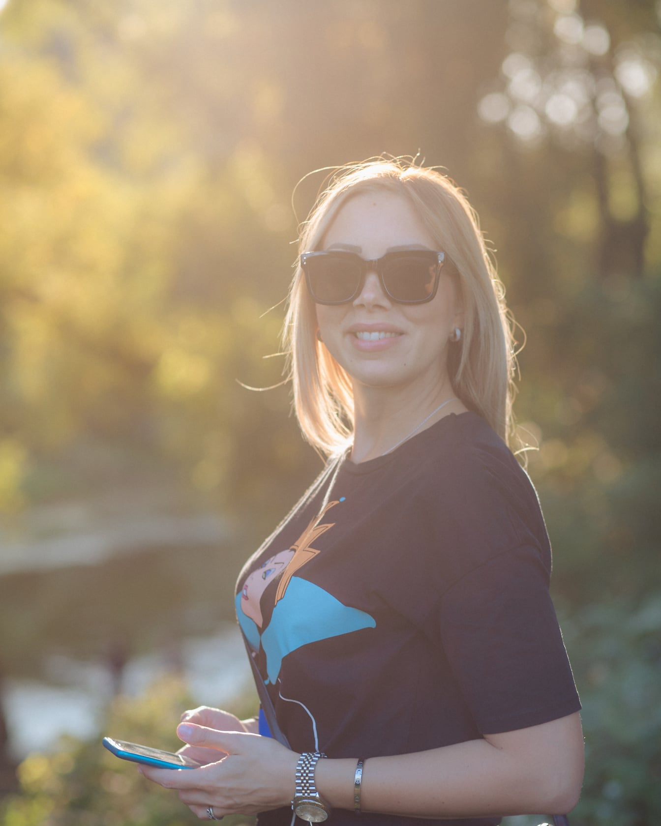Urocza blond kobieta uśmiechnięta w okularach przeciwsłonecznych i promieniach słonecznych w tle