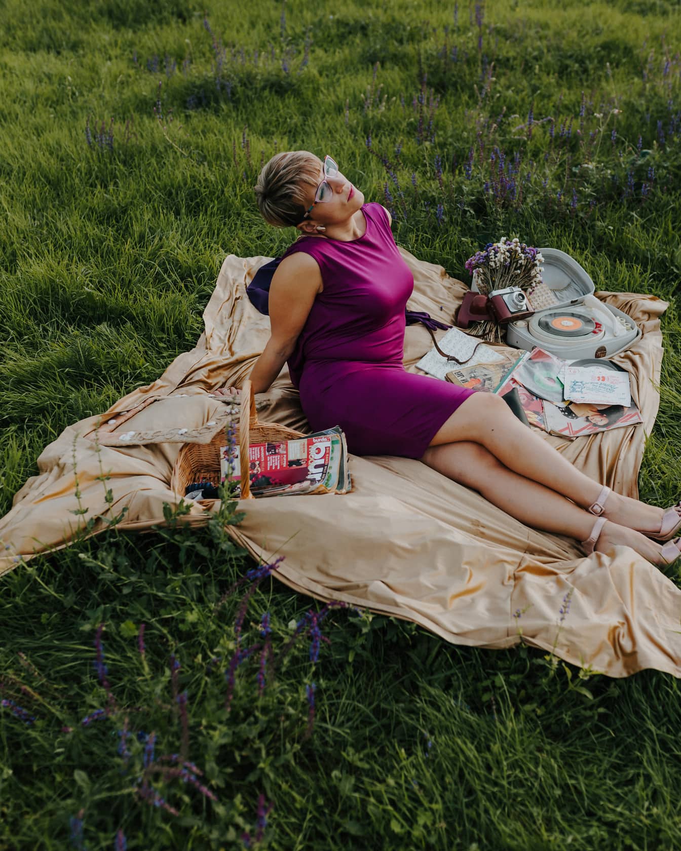 Donna graziosa seduta sulla coperta da picnic in vestito viola