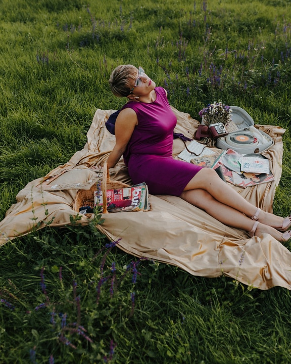 Pretty woman sitting on picnic blanket in purple dress