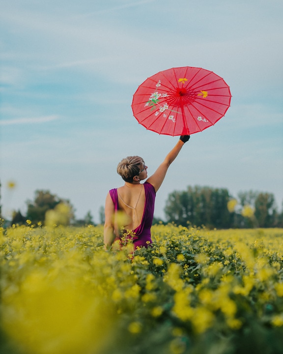 Onnellinen nuori nainen rypsissä vaaleanpunaisella sateenvarjolla