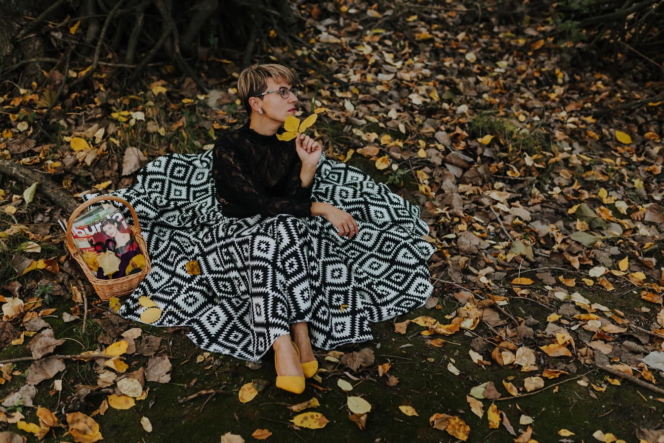 Goed uitziende jonge vrouw in zwart-witte kledingszitting in de herfstbladeren