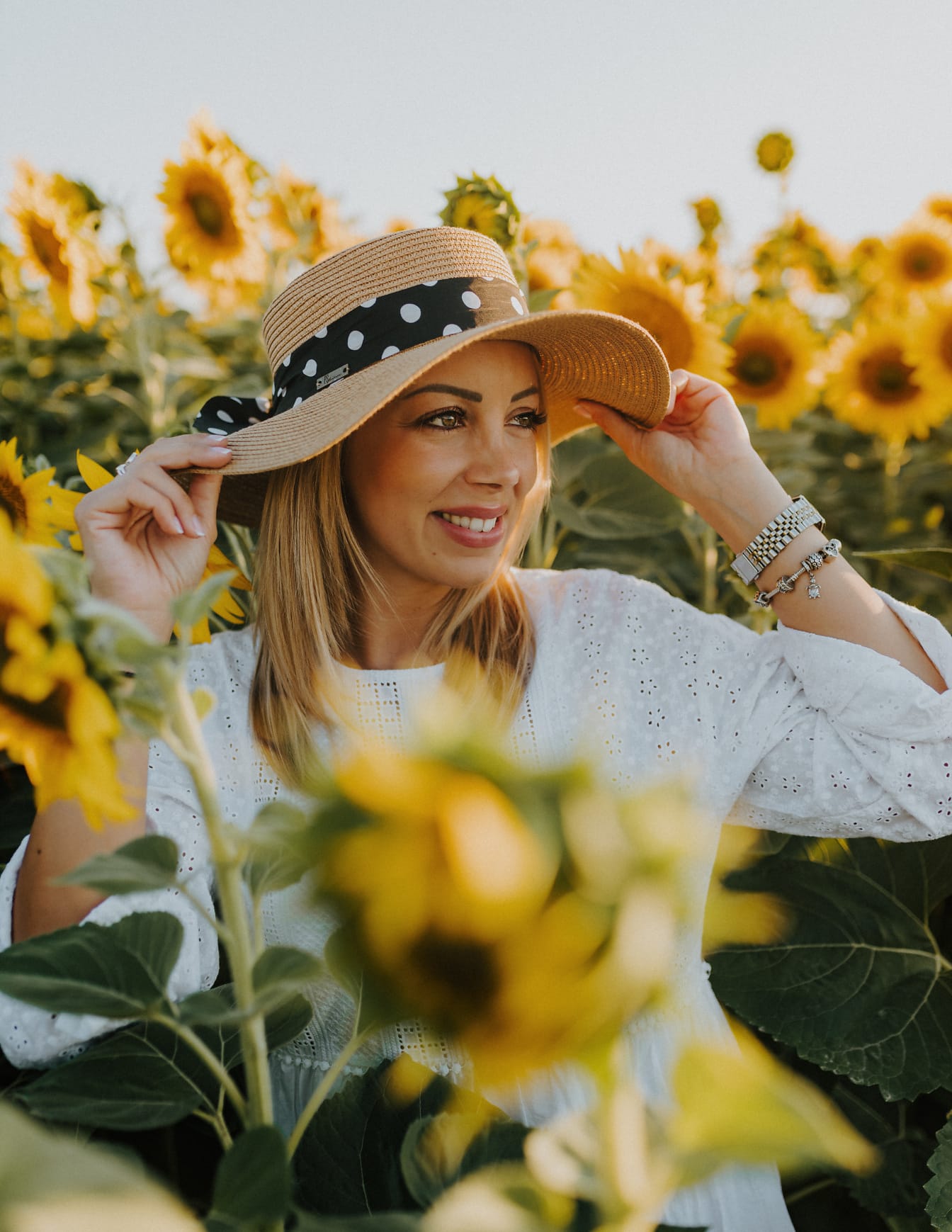 Good looking blonde hair woman in sunflower field with straw hat
