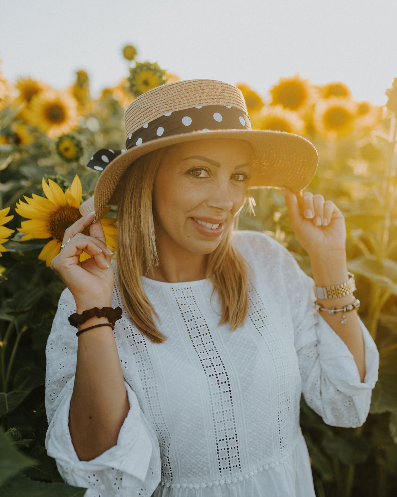 Superbă femeie veselă zâmbind în câmpul de floarea-soarelui cu raze de soare