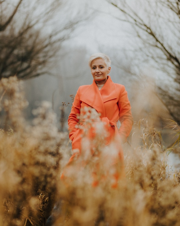 Woman in orange color autumn coat in high grass