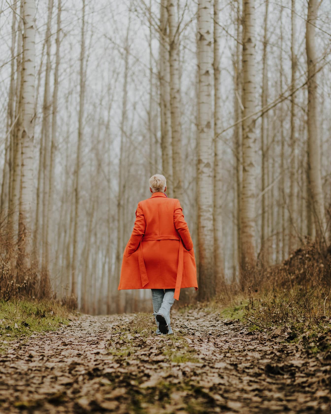Womn muda berjalan di jalur hutan dengan mantel kuning oranye