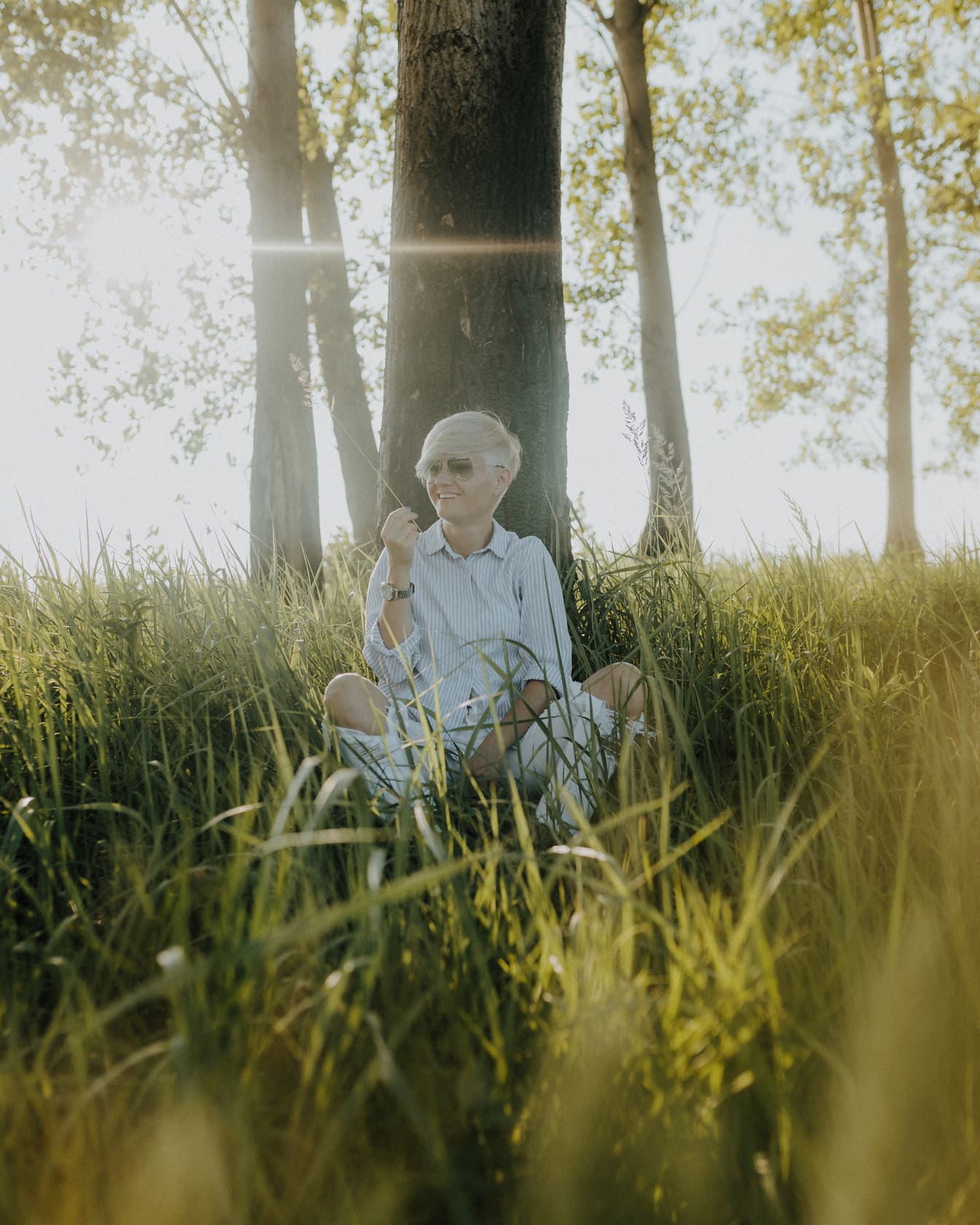 Pirang duduk di padang rumput dan tersenyum dengan sinar matahari di latar belakang