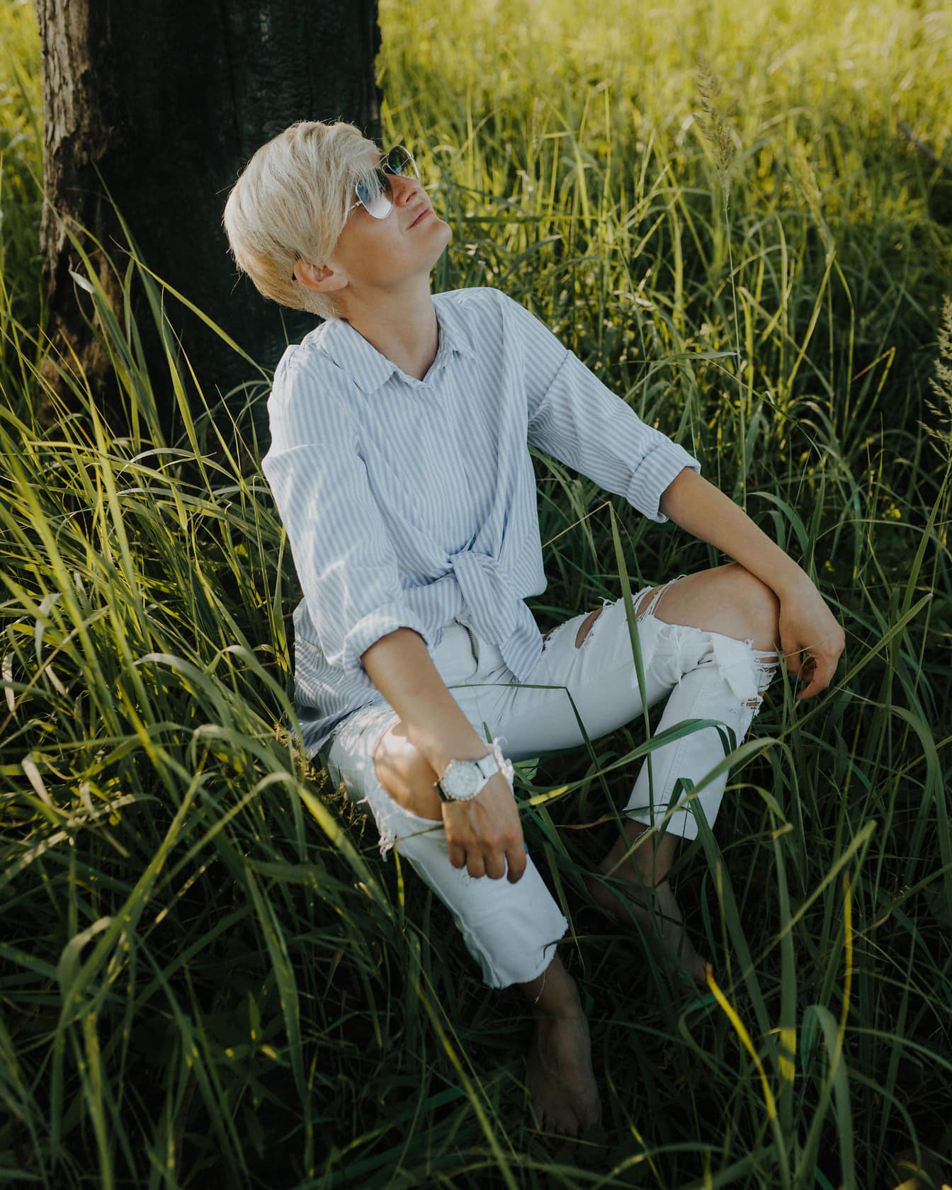 Krátke vlasy blond so slnečnými glaglasami sediacimi v tráve