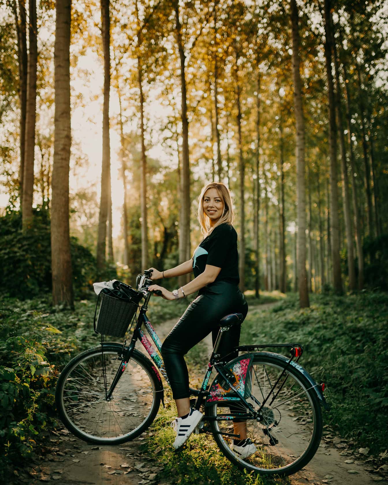 Siyah deri pantolonlu genç kadın orman yolunda bisikletli