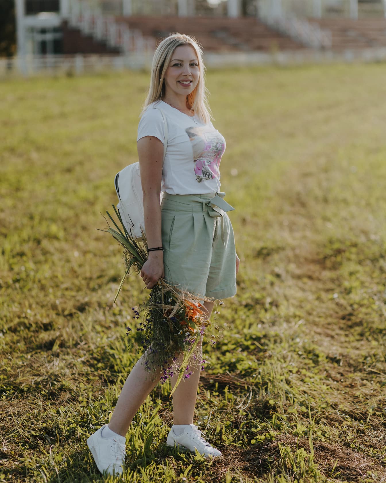 Nádherná blond vlasová žena s kyticou kvetov na poli