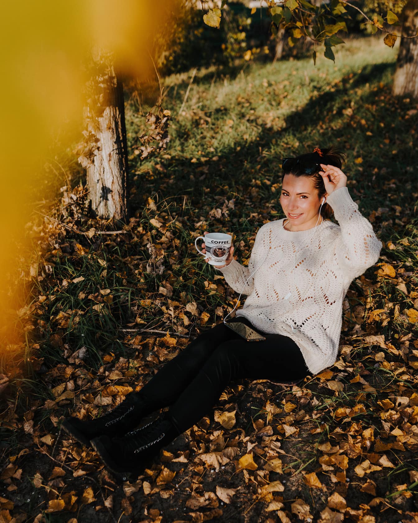 Sonbahar mevsiminde yaprakların üzerinde oturan kahve kupası ile dinlenen bayan