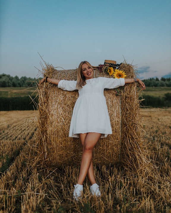 Good looking blonde in white dress at haystack