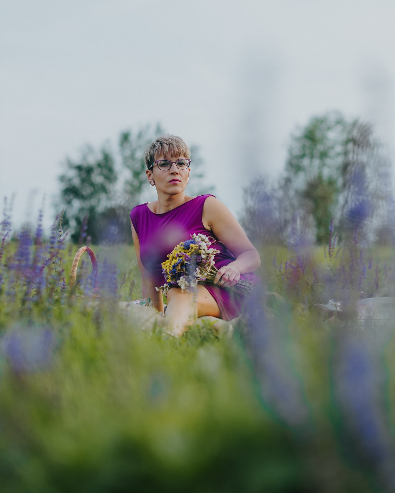 Muotokuva kauniista naisesta violetissa mekossa istumassa niityllä