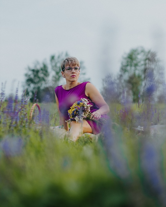 Portrait of pretty lady in purple dress sitting in meadow